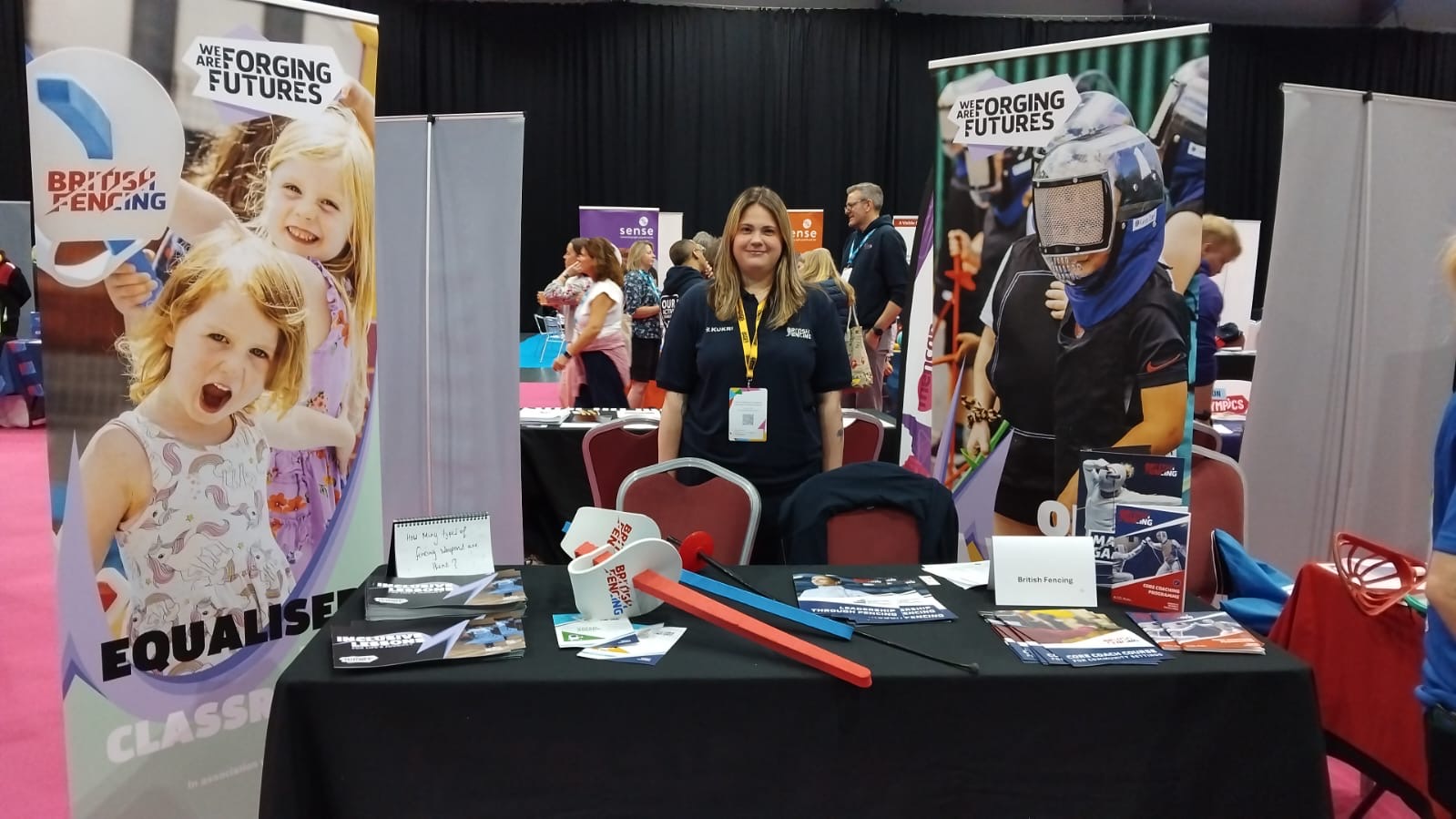 A group of young students holding foam fencing swords smile to the camera